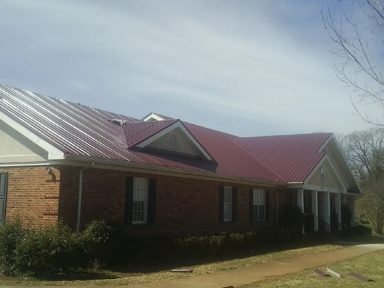 Red metal roof with gabled entries on a long brick building, from a Hail Damage Roof Repair job in Cape May Point