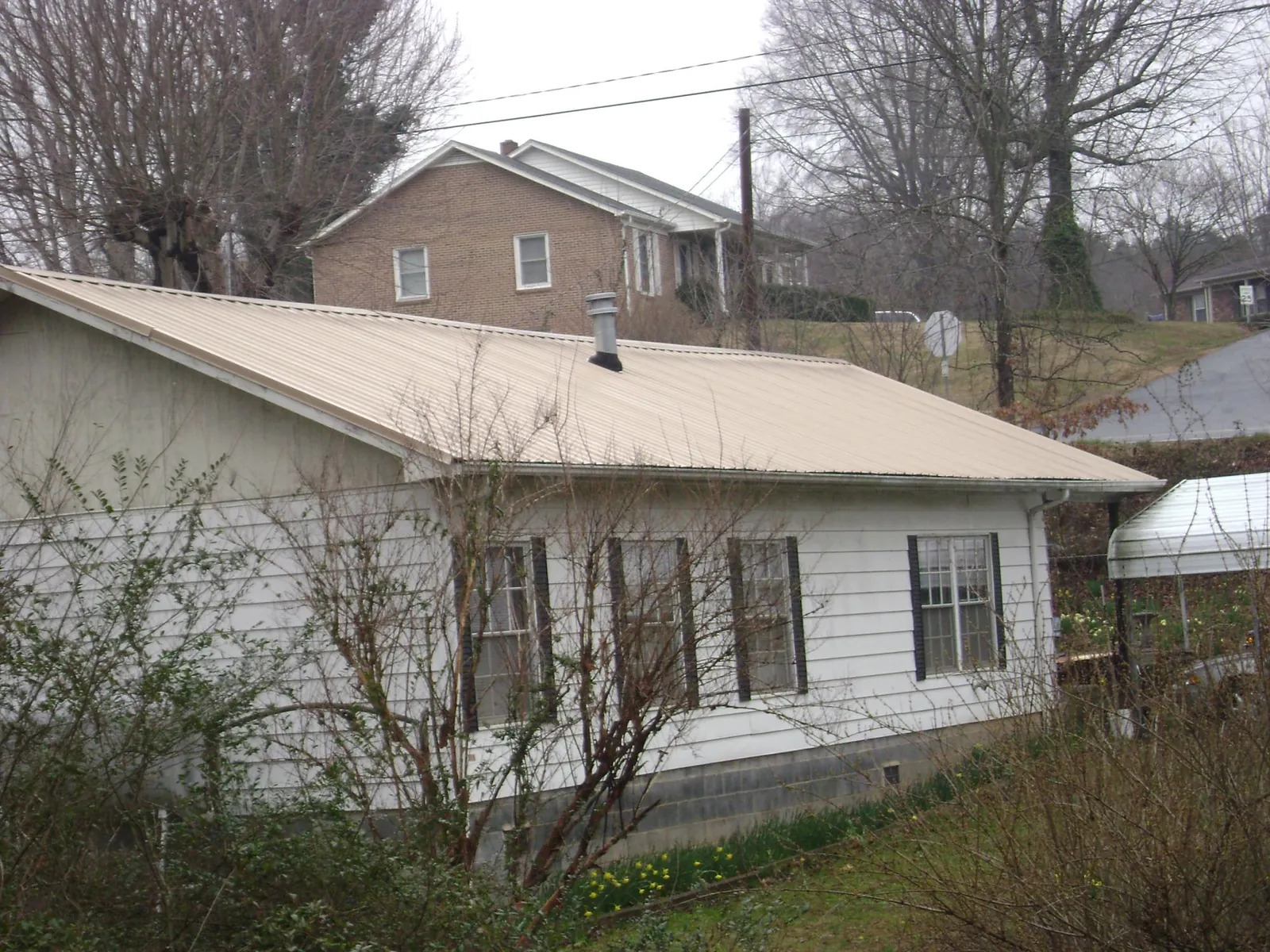 Tan metal roof on a white sided house set into a hillside — Commercial Roofing by Roofing Brothers in Cape May Point
